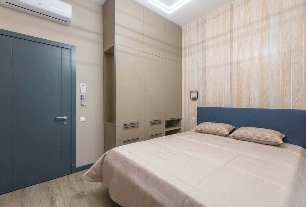 Interior of cozy bedroom with comfortable bed with pillows and coverlet and wardrobe near door